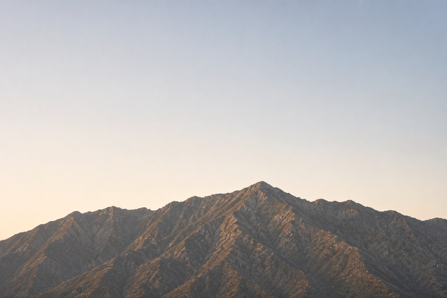 A mountain ridge at first light, its peak catching the sun above a pale sky